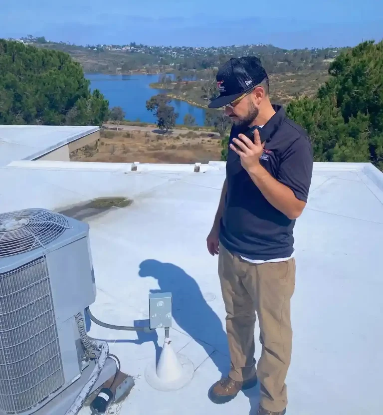 HVAC project manager kevin gonzalez of maximum comfort standing on a roof top on his phone with an AC unit next to him and Lake Murray in the background