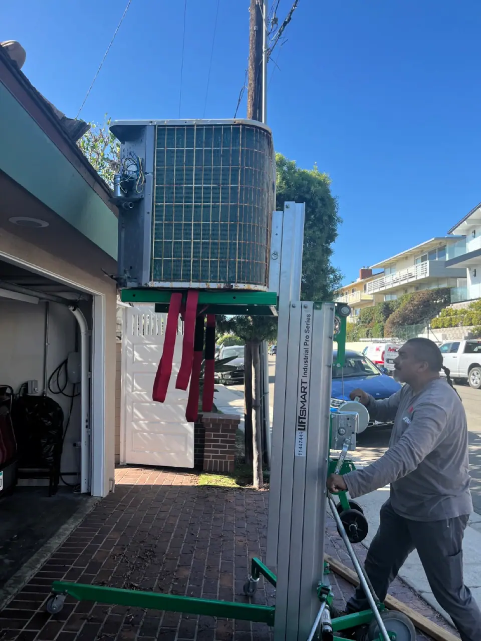 Maximum Comfort technician using a material lift to remove old HVAC equipment at a La Jolla home with overhead utility lines